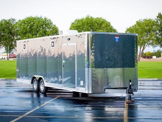 A parked TrailersPlus Enclosed Trailer with trees in the background.