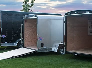 Three TrailersPlus trailers parked side by side in a grassy area.