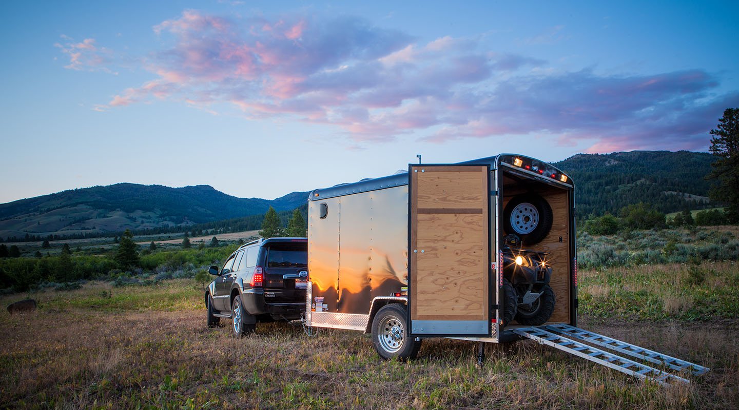Double door cargo trailer parked in a field with ATV driving down the ramp